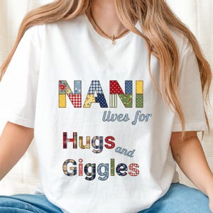 Op de afbeelding: Wit T-shirt met de tekst "NANI lives for Hugs and Giggles". Het woord "NANI" is in een patchwork-ontwerp. De tekst is in een mix van kleuren, waaronder rood, blauw, geel en groen.