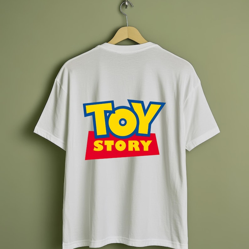 May include: White t-shirt with the "Toy Story" logo on the back. The logo features the words "TOY STORY" in yellow and blue letters on a red rectangle. The shirt is hanging on a wooden hanger.