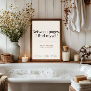 May include: A framed 16x20 digital print with the text "Between pages, I find myself" in a bathroom setting. The print is in a dark brown frame. A vase of flowers, a candle, and a glass jar are on a wooden shelf above a bathtub filled with bubbles.