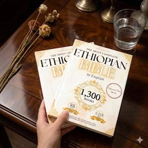 K&ouml;nnte beinhalten: Zwei Exemplare der "The Most Complete Ethiopian Bible" auf Englisch. Die Buchumschl&auml;ge sind cremefarben mit goldenen Buchstaben und Akzenten. Der Text enth&auml;lt "1.300 B&uuml;cher" und "Volume Ten Book".