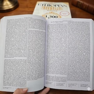 K&ouml;nnte beinhalten: Ein offenes Buch mit Text, mit dem Titel "The First Book of Samuel". Ein zweites Buch mit dem Titel "Ethiopian Bible in English" ist im Hintergrund zu sehen. Das Bild zeigt einen religi&ouml;sen Text.