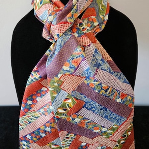 May include: A colorful scarf with a patchwork design. The scarf features a variety of patterns and colors, including red, blue, purple, and green. The scarf is draped over a black mannequin.