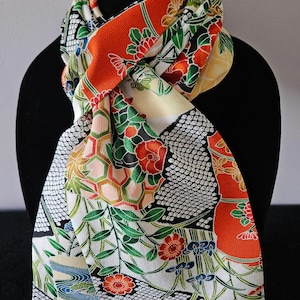 May include: A scarf featuring a vibrant, multi-colored pattern with orange, green, red, and black sections. The fabric displays intricate floral motifs, geometric shapes, and traditional Japanese-inspired designs on a textured, crepe-like surface.