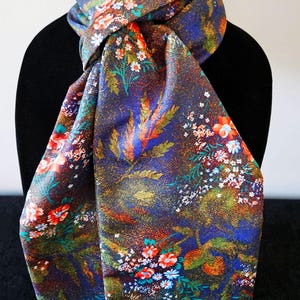 May include: A floral scarf with a dark blue background, adorned with red, orange, and white flowers, and green foliage. The scarf is draped over a black mannequin, showcasing its intricate pattern and color palette.