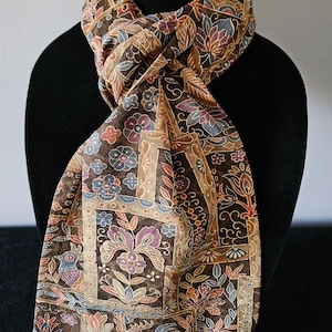 May include: A brown scarf with a floral pattern in shades of blue, purple, and orange. The scarf is draped over a black mannequin head. The scarf's design includes stylized flowers and leaves.