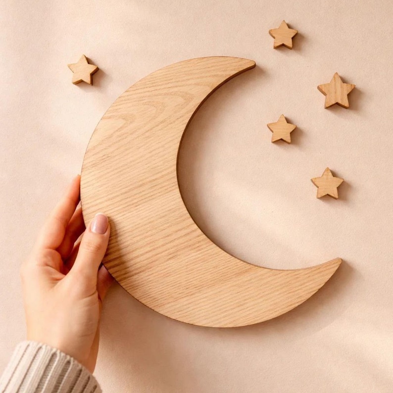 May include: Wooden crescent moon and star wall decor. The moon is a light brown color and is surrounded by five wooden stars. The decor is designed to be mounted on a wall. The background is a light beige color.