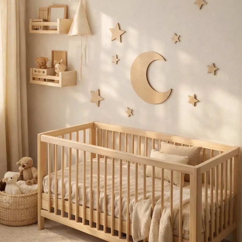 May include: A light wood crib with a neutral-toned bedding set. The nursery features wooden star and moon wall decor. Two small wooden shelves hold decorative items, including teddy bears. A woven basket holds stuffed animals.