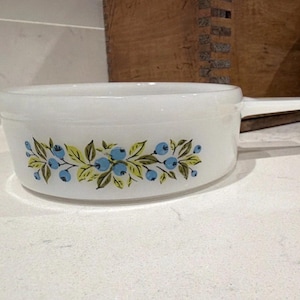 Peut inclure: Plat à four ovale blanc avec une poignée. Le plat présente un motif floral de baies bleues et de feuilles vertes. Le plat est fait d'un matériau épais et opaque, probablement vintage.