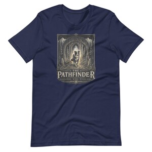 May include: Navy blue t-shirt featuring a detailed graphic of a dog in a forest, with the text "THE PATHFINDER" and the words "LOYAL. WISE. WILD." The design is in shades of gray and beige.
