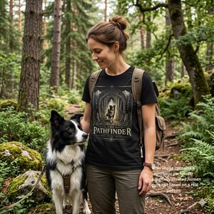 May include: Black t-shirt with "THE PATHFINDER" graphic featuring a dog in a forest scene. The shirt is worn by a person with a backpack, standing next to a black and white dog in a forest setting. The text "LOYAL. WILD. WILD." is below the graphic.