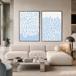 Könnte beinhalten: Zwei gerahmte abstrakte Kunstdrucke. Jeder hat einen schwarzen Rahmen mit einem hellblauen und weißen organischen Muster. Das Kunstwerk wird über einem cremefarbenen Sofa in einem modernen Wohnzimmer präsentiert.