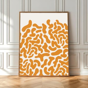 Könnte beinhalten: Ein gerahmter Kunstdruck mit einem abstrakten Muster aus orangefarbenen organischen Formen auf weißem Hintergrund. Das Kunstwerk ist in einem Holzrahmen eingefasst und bietet eine moderne, minimalistische Ästhetik. Der Druck wird auf einem Holzboden präsentiert.
