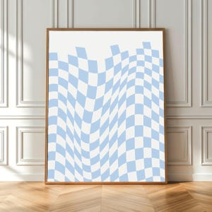 Könnte beinhalten: Ein gerahmter Kunstdruck mit einem wellenförmigen, hellblauen und weißen Schachbrettmuster. Das Kunstwerk wird in einem Holzrahmen präsentiert und lehnt an einer weißen Wand mit Zierleisten, was eine moderne Ästhetik schafft.