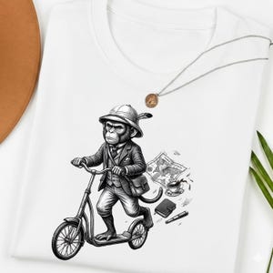 Puede incluir: Camiseta blanca con una ilustración en blanco y negro de un mono con traje montado en un patinete. El mono lleva sombrero y maletín. También se muestra un mapa, una taza de café y otros objetos.
