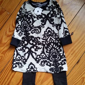 Baby jersey fabric dress in black and cream dainty damask print with matching black knit leggings with long sleeves and black trim. Size 2T