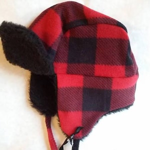 Pode incluir: Chapéu trapper xadrez vermelho e preto com aba de orelha de pele sintética preta.