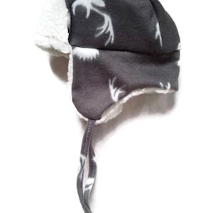 May include: Grey fleece winter hat with a white faux fur trim and a white deer print. The hat has a long grey string tie.