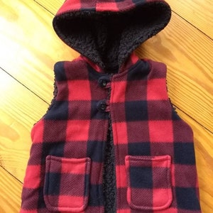 Buffalo plaid hooded red and black fleece vest lined with faux black sherpa. Gender neutral. Button closure.