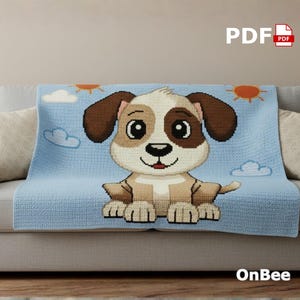 May include: A light blue crocheted blanket featuring a cartoon puppy with brown and white fur, sitting on a light blue background with clouds and suns. The blanket is draped over a gray sofa with beige pillows. The text "OnBee" is in the bottom right corner.
