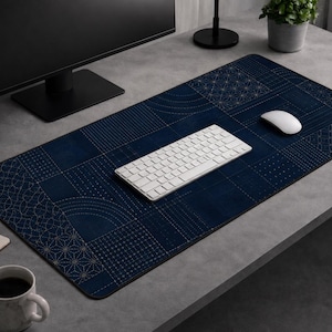 May include: A navy blue desk mat with a geometric pattern in gold and white. A white keyboard and mouse sit on the mat. The mat is rectangular and covers a large portion of the desk surface.