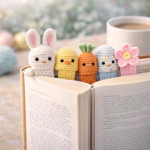 以下が含まれることがあります： ウサギ、ヒヨコ、ニンジン、鳥、花の形をした、手作りのかぎ針編みのブックマーク5個セット。ウサギはピンクの耳の白い色、ヒヨコは黄色、ニンジンはオレンジ色、鳥は青と白、花はピンク色です。開いた本の中に置かれています。