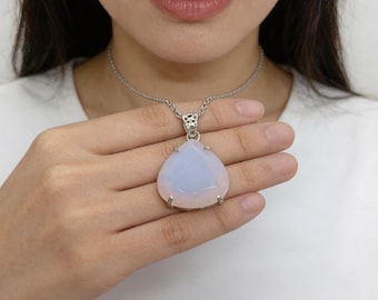 May include: A silver necklace with a large, pear-shaped, pale blue and pink gemstone pendant. The pendant is held in a silver setting and hangs from a delicate silver chain. The necklace is displayed on a person's hand.