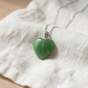 Heart shaped green fluorite pendant necklace displayed on fabric background highlighting natural crystal beauty.