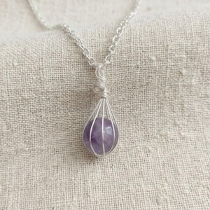 Purple amethyst sphere pendant necklace displayed on neutral fabric background, highlighting polished finish and handcrafted silver wrap.