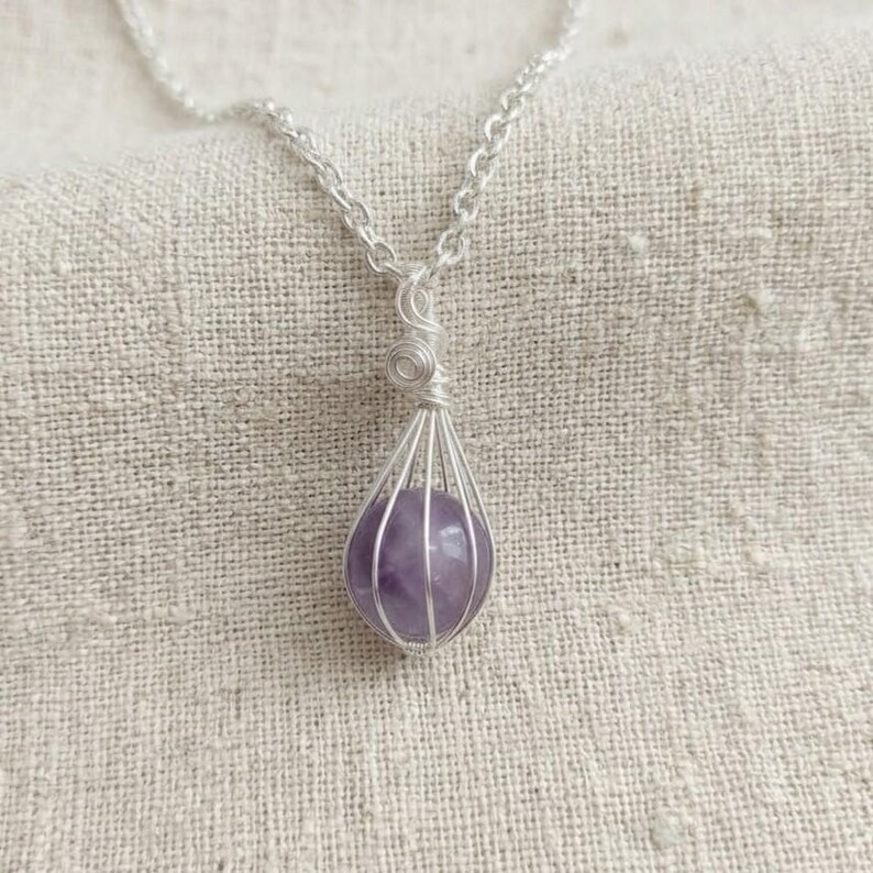 Purple amethyst sphere pendant necklace displayed on neutral fabric background, highlighting polished finish and handcrafted silver wrap.