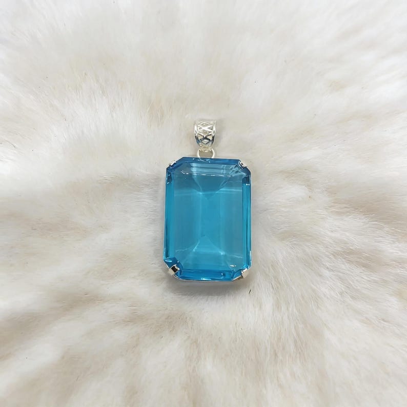 Close-up of natural blue topaz emerald shape pendant showcasing bright Swiss blue color and sterling silver setting, perfect healing crystal necklace for throat chakra jewelry.