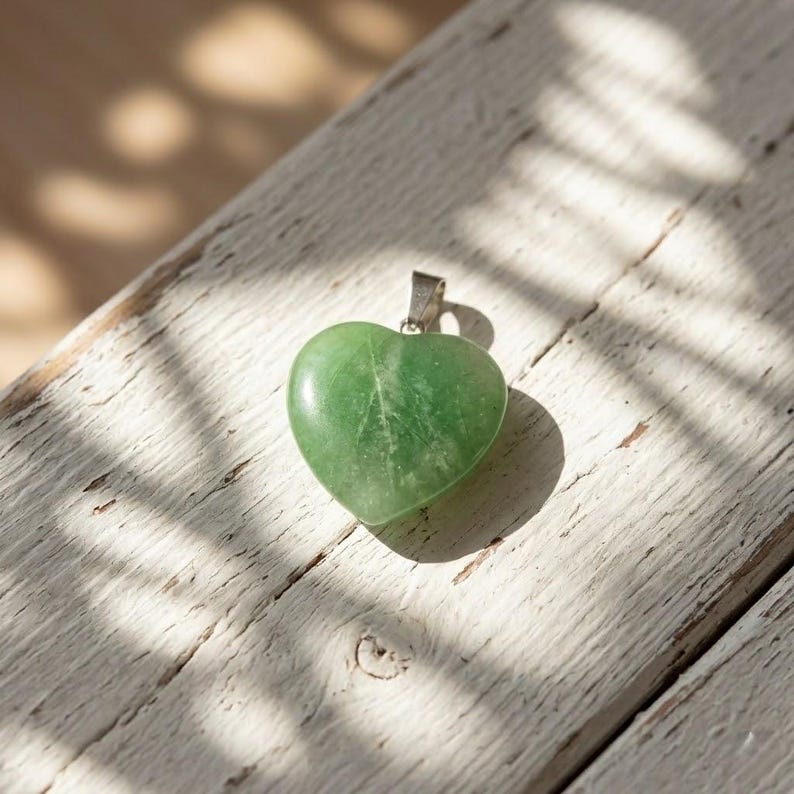 Close up of natural green fluorite heart shaped crystal pendant with smooth polished finish and silver chain, ideal for emotional healing necklace.