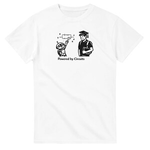 以下が含まれることがあります： 白のTシャツ。黒と白のグラフィックで、ロボットと卒業生が描かれています。ロボットは回路図を指し、卒業生は本を持っています。「Powered by Circuits」の文字が下にあります。