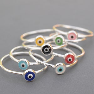 May include: A set of silver rings with colorful evil eye charms. The rings are stacked on top of each other, with the charms facing up. The charms are in various colors, including blue, green, red, yellow, and black.