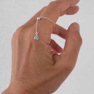 May include: A silver ring with a dangling turquoise evil eye charm. The ring is on a person's finger.