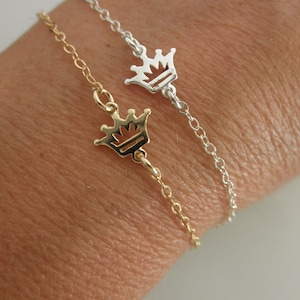 May include: Two delicate bracelets with crown charms. One bracelet is gold and the other is silver.