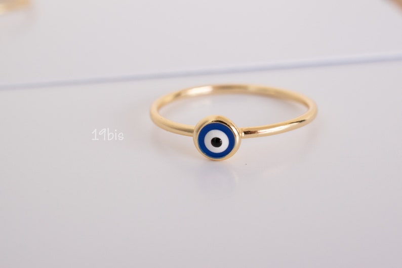 Peut inclure: Une bague en or avec un charme &oelig;il bleu et blanc. La bague est une bande simple avec un petit charme rond au centre.