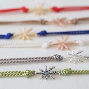 May include: A set of six bracelets with different colored cords and silver star-shaped charms. The charms are all the same design, but they are made of different metals.