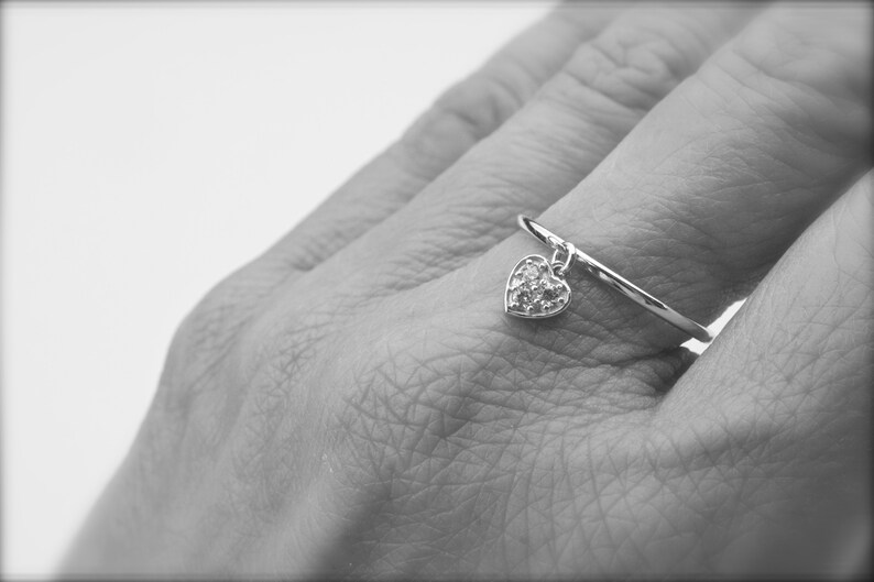 May include: A silver ring with a dangling heart charm. The heart is covered in small, sparkling stones.