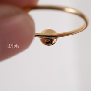 Peut inclure: Une bague en or avec une bande ronde et lisse et une petite perle ronde au sommet. La perle est estampill&eacute;e du num&eacute;ro "925".
