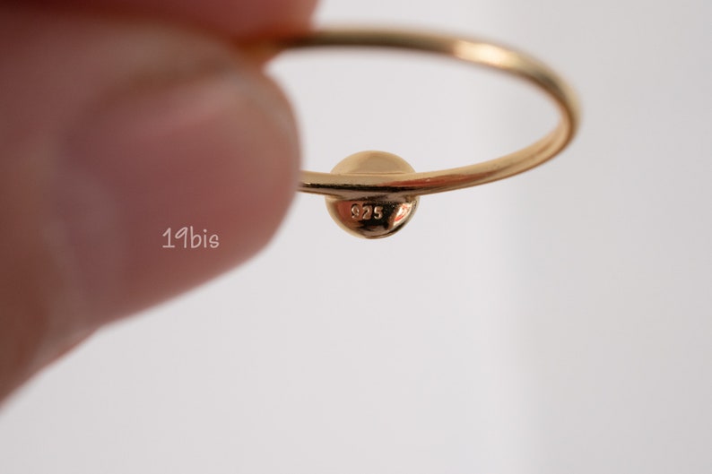 Peut inclure: Une bague en or avec une bande ronde et lisse et une petite perle ronde au sommet. La perle est estampill&eacute;e du num&eacute;ro "925".