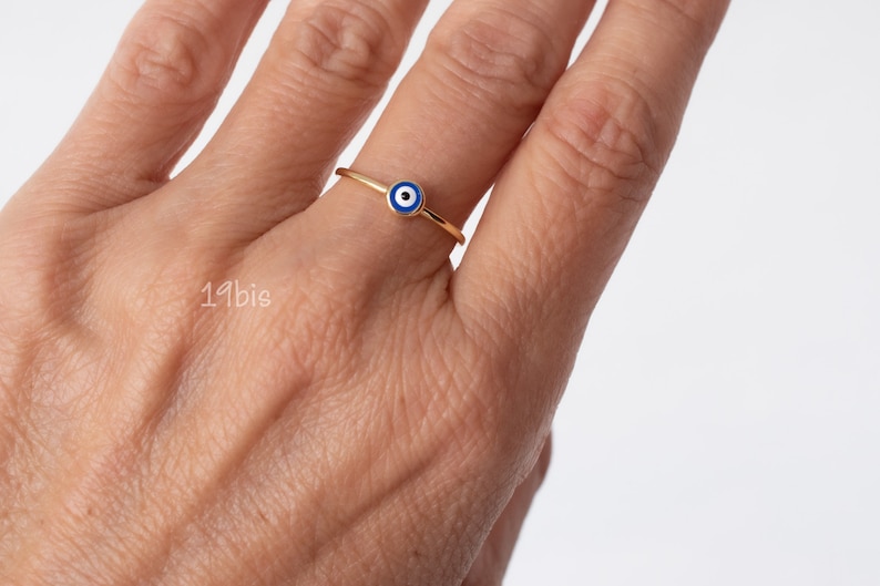 Peut inclure: Une bague en or avec un charme &oelig;il turc bleu et blanc. La bague est port&eacute;e sur un doigt.