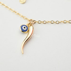 May include: Gold chain necklace with a blue evil eye charm and a gold horn charm.