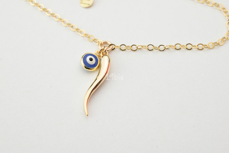 May include: Gold chain necklace with a blue evil eye charm and a gold horn charm.