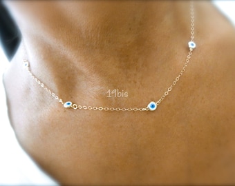 May include: A delicate gold chain necklace with four small blue evil eye charms. The necklace is worn on a person's neck.