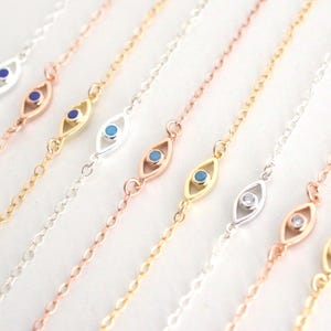 May include: Close-up of several delicate chain bracelets. Each bracelet features an eye-shaped charm with a blue or clear center. The bracelets are in various metallic finishes, including gold, silver, and rose gold.