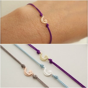 May include: Three friendship bracelets with a crescent moon and star charm. The bracelets are made with purple, light blue, and gray cord.