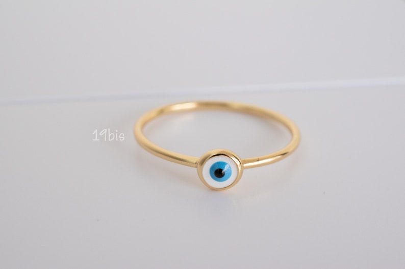 Peut inclure: Une bague en or avec un charme &oelig;il bleu et blanc. La bague est une bande simple avec un charme rond au centre.