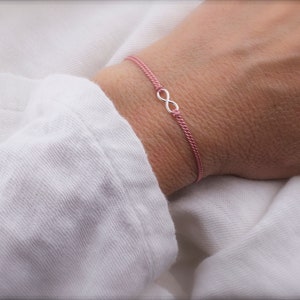 May include: A pink string bracelet with a silver infinity symbol charm.
