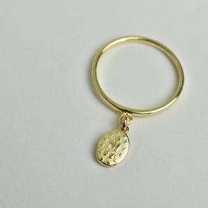 Peut inclure: Une bague en or avec un petit pendentif de forme ovale suspendu. Le pendentif a une surface textur&eacute;e.