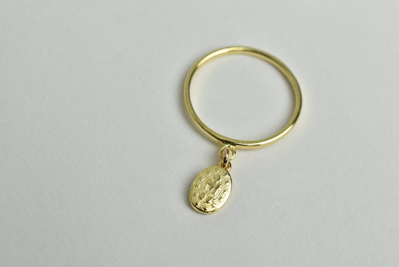 Peut inclure: Une bague en or avec un petit pendentif de forme ovale suspendu. Le pendentif a une surface textur&eacute;e.